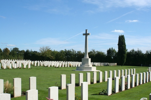 Rows of white crosses between mown grass with the white Cross of Sacrifice in the background. Trees can be seen in the distance