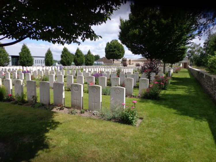 Rows of white gravestones with plants in front and areas of mown grass. Trees surround the cemetery