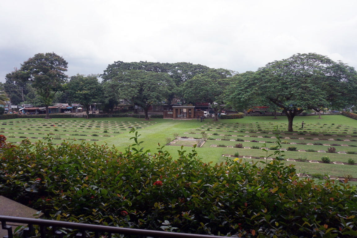 Maynamati War Cemetery with a hedge in the foreground and rows of gravestones behind