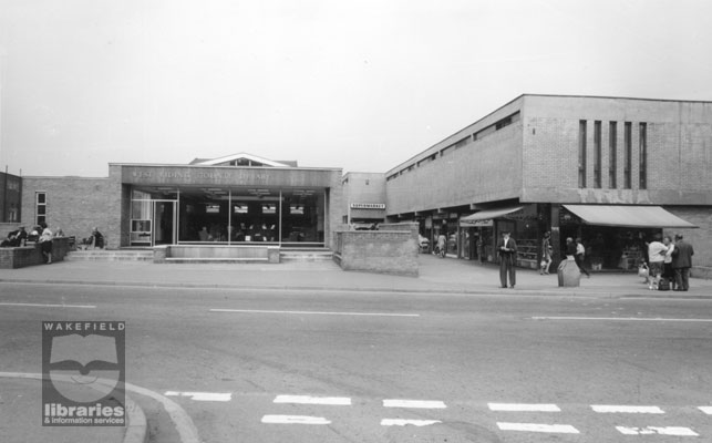 A black and white photograph of South Elmsall Library and Queens and Asda Supermarket, South Elmsall.  The library was opened in 1966.  Whilst now known as South Elmsall Library this was County Library, Barnsley Road, Moorthorpe. The supermarket, which stood on the site of the Old Palace Picture House, later became a Netto supermarket.  The shop on the right corner was a fruiterer, with a cafe next door.  Internal Reference: WR (LS) Frith Collection 