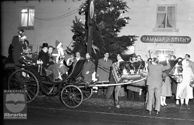 A black and white negative of Father Christmas in a horse drawn carriage outside the Hammer and Stithy public house, Ossett.  The horse has been fitted with reindeer antlers.  A decorated Christmas tree stands behind them.  Internal Reference: OS FOW 255