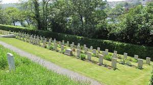 Photo of Falmouth Cemetery. Rows of headstones in front of a hedge and line of trees.