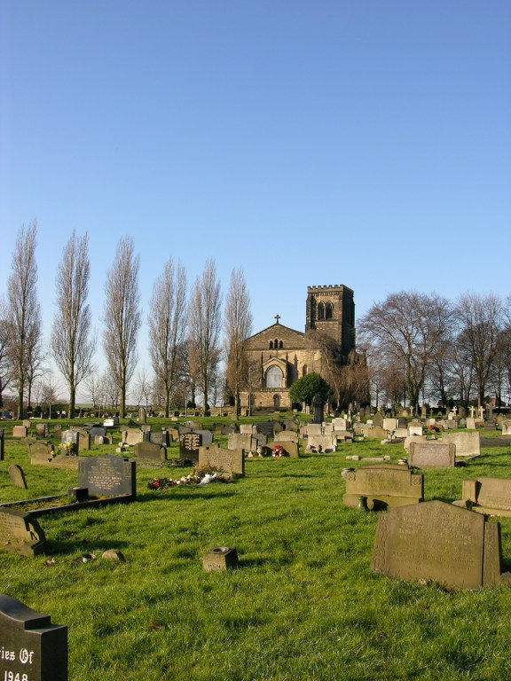 Photo of Alverthorpe Churchyard. A graveyard with headstones and a chapel and trees in the background.