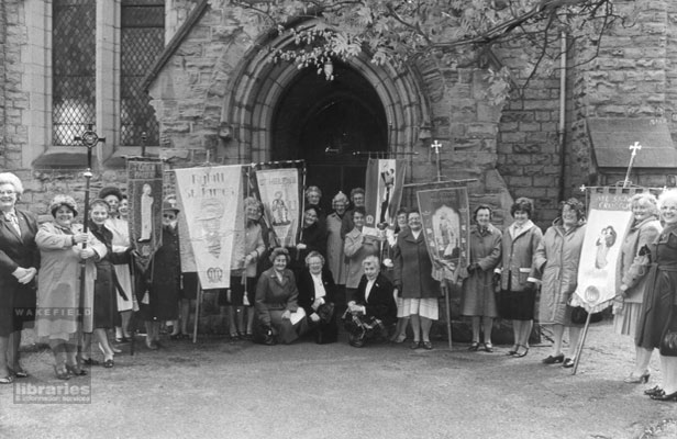 A black and white photograph showing members of the Chevet Deanery Mothers Union outside Saint Catherine Church on Doncaster Road, Belle Vue in May 1983.  The ladies are holding banners outside the entrance.  The church was destroyed by fire in 1993 and a new church was built incorporating some of the old church in 1995. Internal Reference: WR 38 060 (Wakefield Express Picture Reference Number W/4054/1)