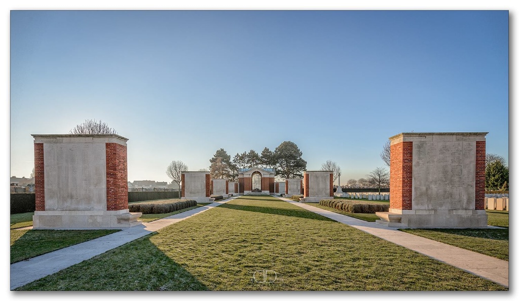 Photo of Dunkirk memorial. A central grass path lined with 8 red brick and white stone wall memorials with a central red brick and white stone memorial.