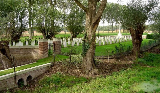 The entrance to Hospital Farm Cemetery. Trees and gravestones can be seen