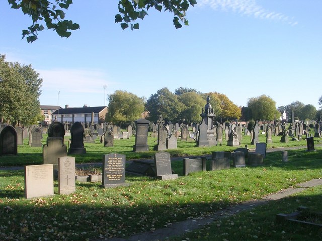 Photo of Wakefield Cemetery. Grassed area with headstones and a line of trees in the background.