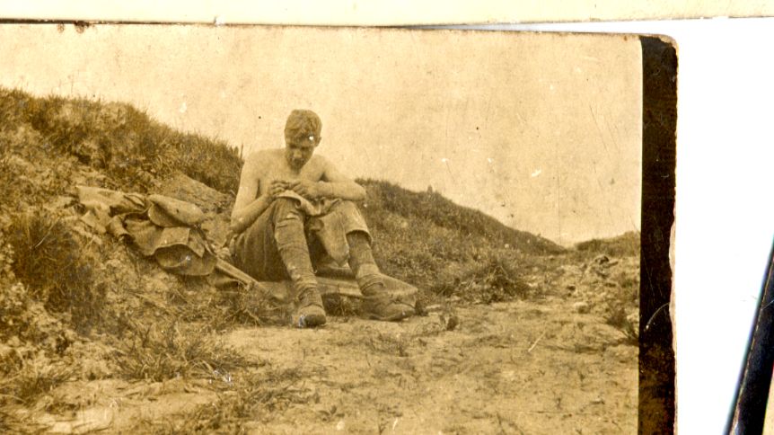 a soldier is sitting on the ground writing a letter. he has taken his jacket off