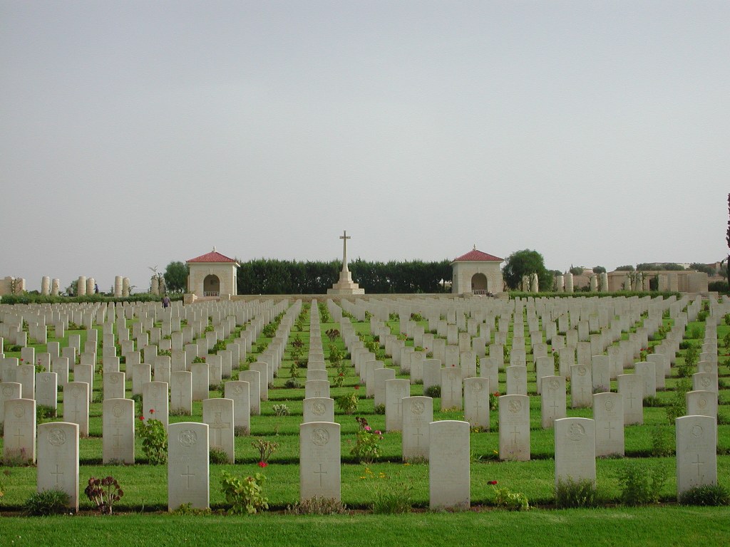 Massicault War Cemetery with a large number of gravestones in rows  running up a hill towards a large cross