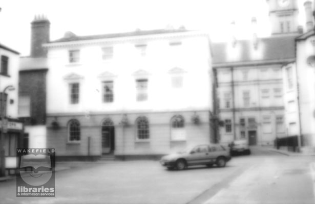 A black and white photograph showing Vicars Orriss estate agents on Crown Court, Wakefield, in 1996.  This was once a wool staplers warehouse.  The side of the Town Hall on Lee Street can be seen in the background.  Internal Reference: WR BIRD STREET SURVEY: L29