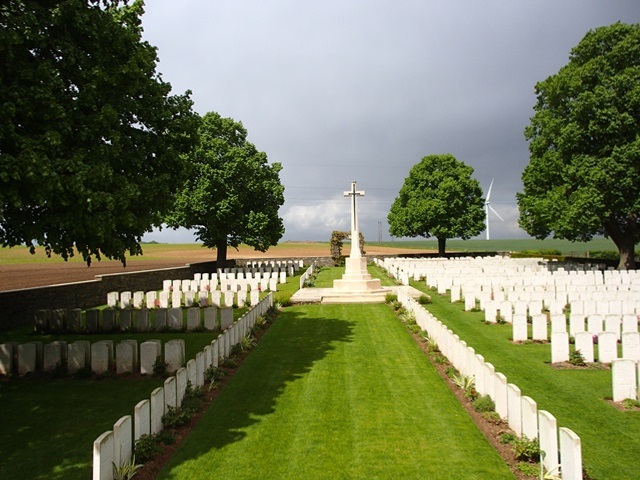 Photo of Achiet-le-Grand Communal Cemetery Extension. Rows of white headstones with a grass path to a large white stone cross monument.