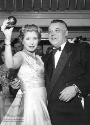 A black and white photograph of Lady Docker, in Castleford for the charity taws contest, the 'Reight Neet Aht'.  With her is Sid Colclough, who was responsible for organising the events.  Lady Docker holds a specially made 'taw', or marbles.  Internal Reference: CA Reight Neet Aht Coll