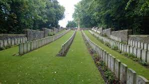 Photo of Roeux British Cemetery. Rows of headstones on grass with trees in the background.