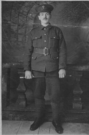 Bertram Morrell standing in his army uniform and wearing a cap. he holds a stick in his hand