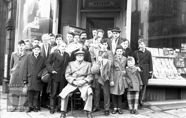 A black and white negative of a large group of people at the front of Smiths newsagent, sited at the junction of Station Road and Prospect Road, Ossett.  Internal Reference: OS FOW 520