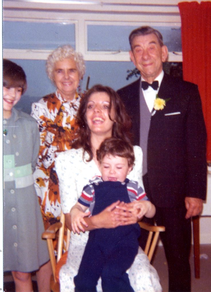 colour photograph of john dressed smartly with a bow tie and his wife stands next to him in front it a woman holding a young boy and another girls stands next to her