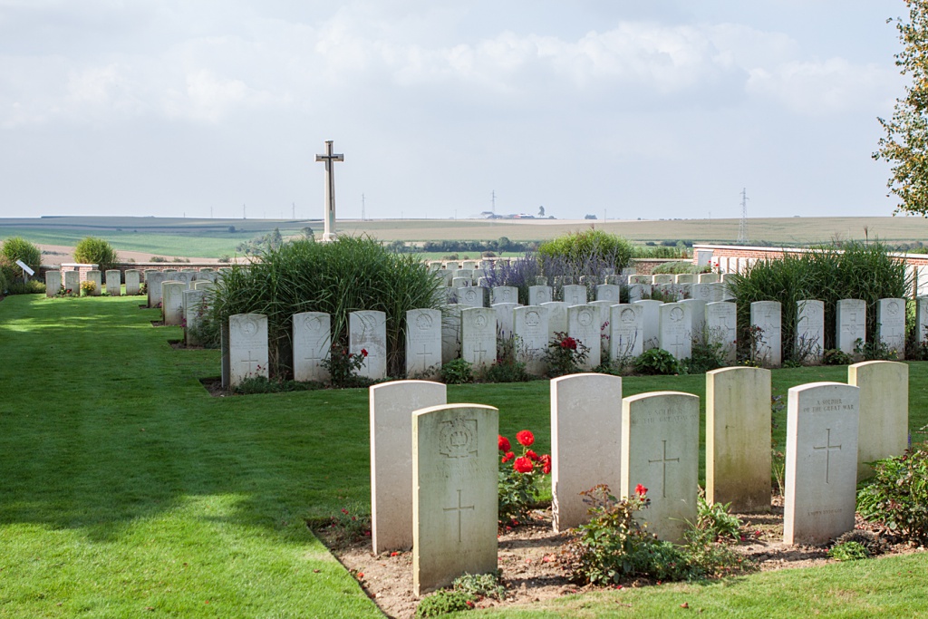 Photo of Le Cateau Military Cemetery. Rows of haedstones in front of a cross memorial.