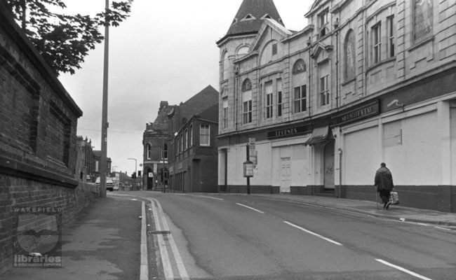 A black and white photograph of Station Road, Castleford, in 2000.  Legends Nightclub is on the right and in the background, after crossing Carlton Street at the traffic lights, Bank Street can be seen.  Internal Reference: CA YILLUS 4572