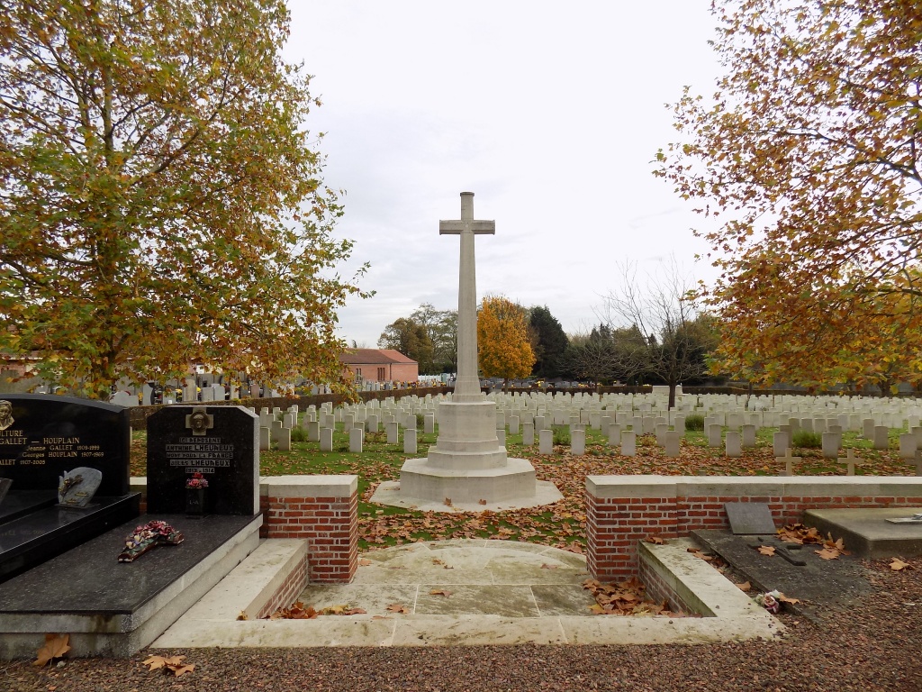 steps lead down to the large white cross of sacrifice flanked by trees and rows of white gravestones are beyond
