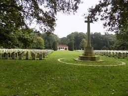 a white cross of sacrifice surrounded by mown grass with rows of gravestones to the left and right