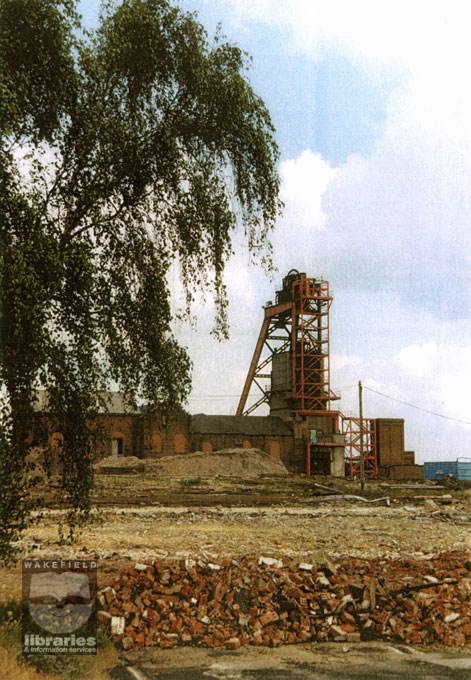 A colour copy of a photograph of Sharlston Colliery, whilst it was undergoing demolition at the end of its life as a pit.  Heaps of rubble can be seen in the foreground and the winding gear, still standing, dominates the picture.  Internal Reference: WR (LS) Sharlston Collection