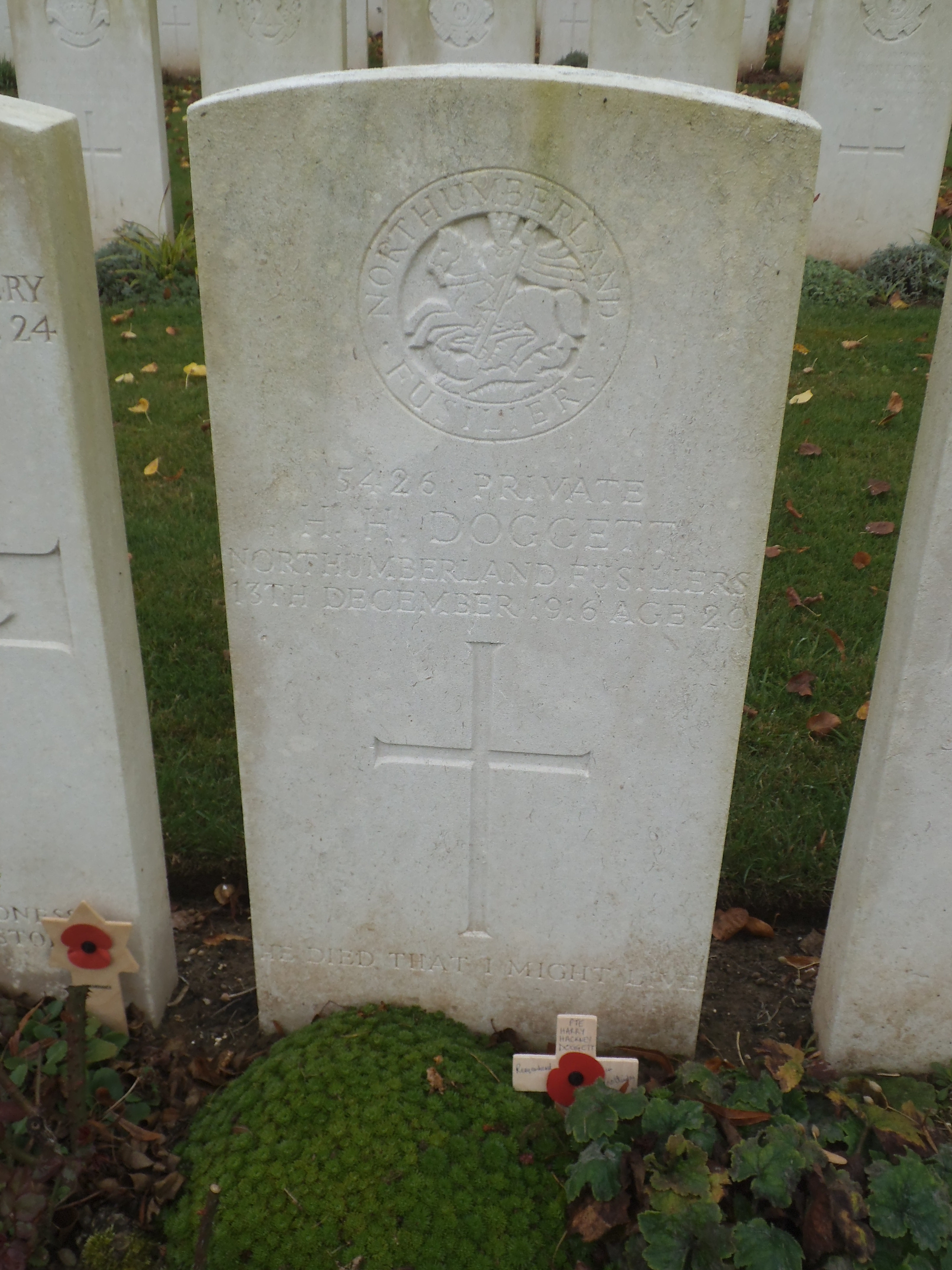 the white gravestone close up of his grave which has the northumberland fusiliers emblem at the top and the words inscribed below read 5426 private h h doggett northumberland fusiliers 13th december 1916 age 20 he died that i might live