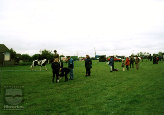 A colour photograph showing members of Castleford Riding Club at an event in Queen's Park in 2000.  Horse boxes are packed behind the area where a rider is chatting to bystanders.  Another pony and rider are in the centre of the arena.  Internal Reference: CA YILLUS 5514