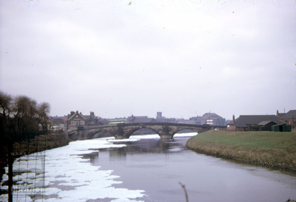 A colour slide showing foam on the River Aire at Castleford.  The foam was caused by detergents deposited in the river by textile mills, activated by the weir.  Also in the photograph is Hartley's Bridge, built by Jesse Hartley in 1808, which replaced a seven arched wooden construct.  On the right hand side of the bridge is Ship Inn, with Hartley's warehouse on the left of the picture.  All Saints Parish Church and Allinsons flour mill can also be seen.  Internal Reference: Castleford and District Historic