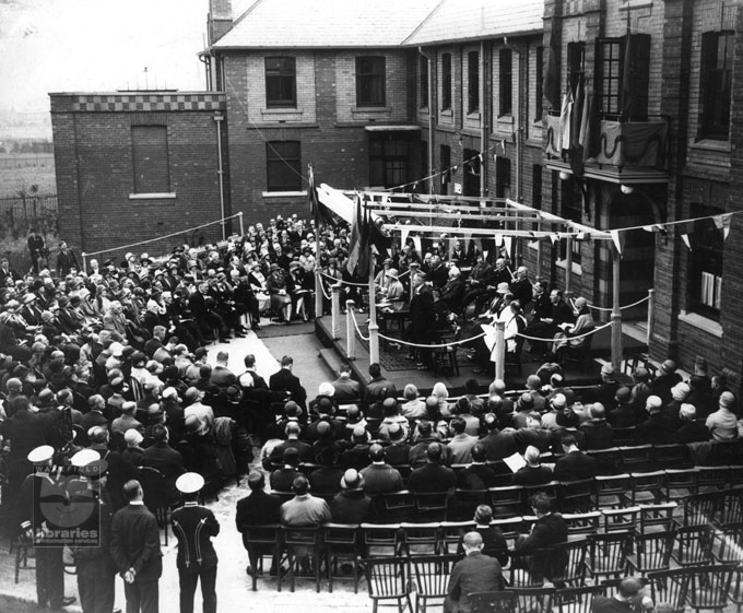 A black and white photograph of the official opening of Castleford and Normanton District Hospital, showing Princess Mary and local dignitaries on a platform in front of the main entrance.  All around them people are seated observing the proceedings.  This hospital was financed by collections in factories and mines, fundraising events and donations from private individuals.  Internal Reference: CA YILLUS 2418