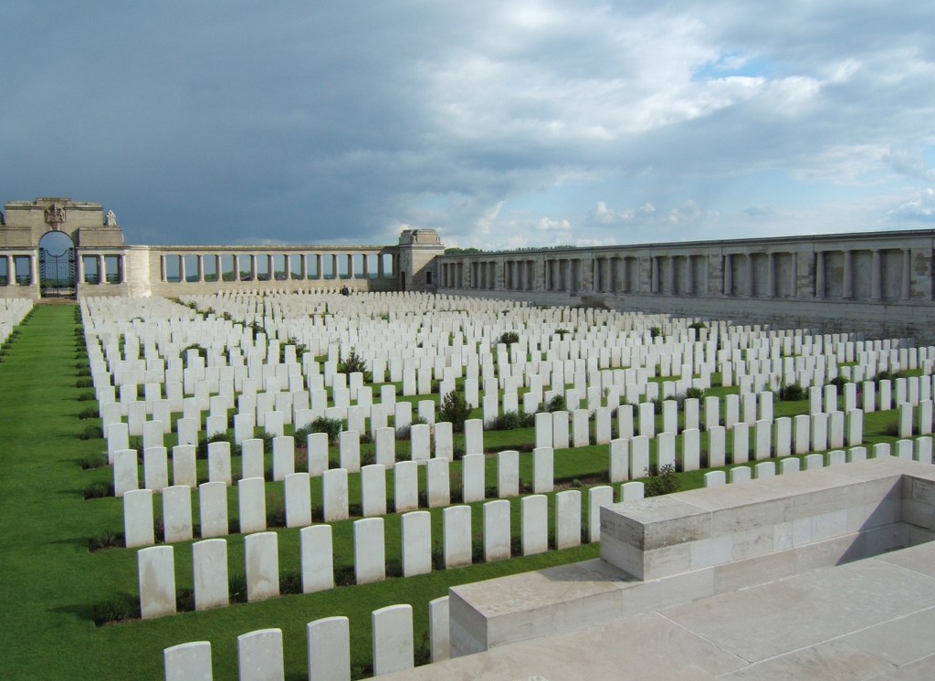 Photo of Pozieres British Cemetery. Rows of white stone headstones surrounded by a wall of columns.