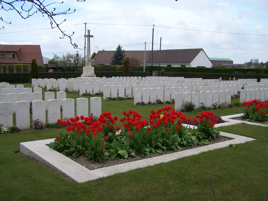 Esquelbecq Military Cemetery with flowers at the front and rows of gravestones behind