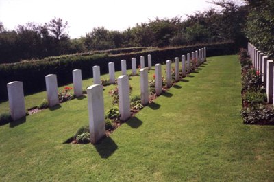 Rows of white gravestones with plants in front of them between areas of mown grass. The cemetery is surrounded by a hedge
