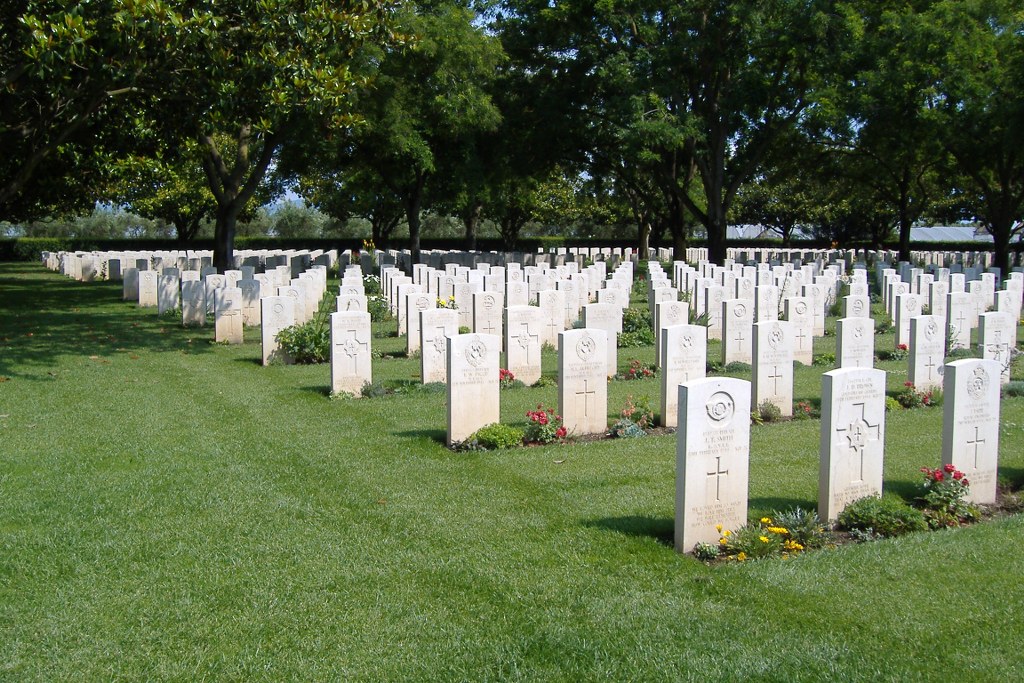 rows of white gravestones between mown grass with trees in the background