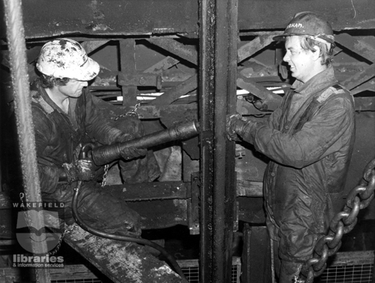 A black and white photograph showing two shaftsmen working on the shafts at Sharlston Colliery in 1982.  The work was part of a £10 million scheme to boost production to a million tonnes of coal a year.  The investment programme was to install new headgear to deal with the larger coal skips, and build an underground bunker to store 1000 tonnes of coal.  The pit was expected to have a life of 25 years after the improvement.  It closed in the 1990s.  Internal Reference: WR