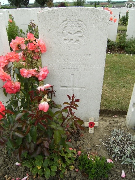 aaron smeaton's white gravestone inscribed with his regimental badge, his details and a cross. a flowering plant is next to the grave